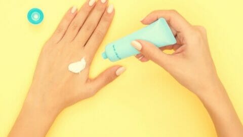 person putting sunscreen on their hand with yellow background