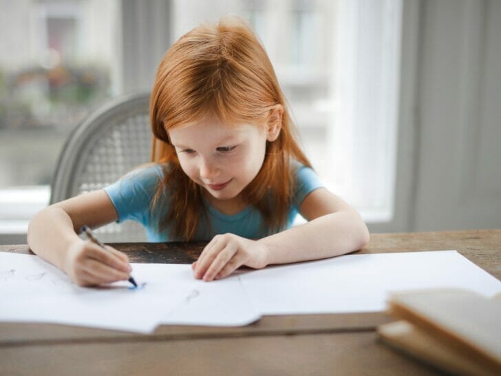 Diligent small girl drawing on paper in light living room at home