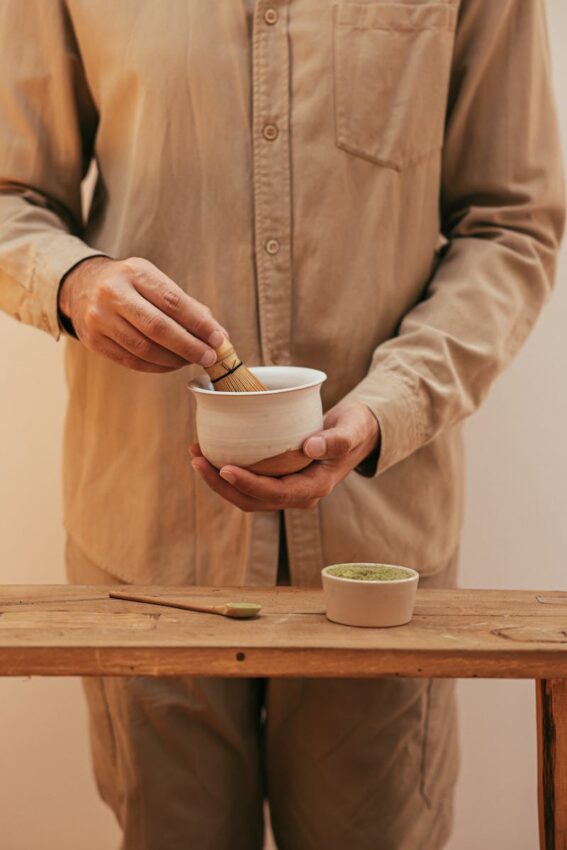 Close-up of a person preparing matcha with a bamboo whisk, showcasing traditional tea ceremony elements.