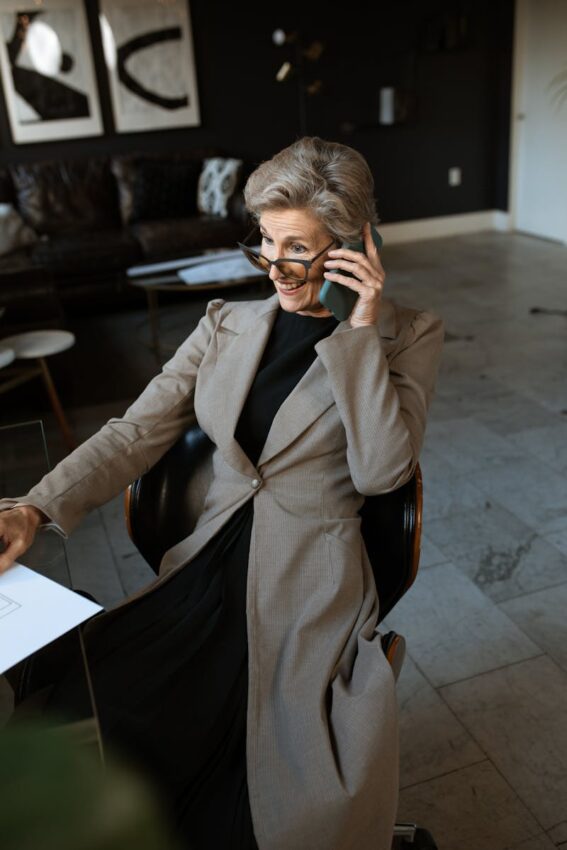 Elegant senior woman in gray coat using a cellphone in a modern office.