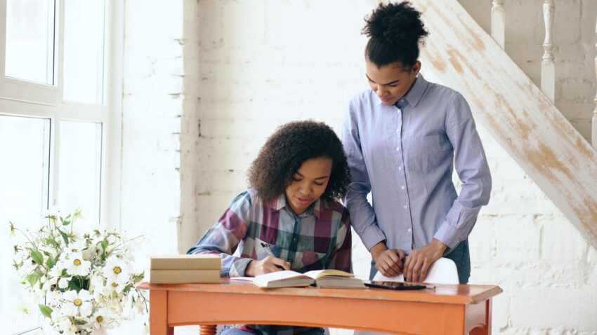 Woman helps girl with homework at desk.