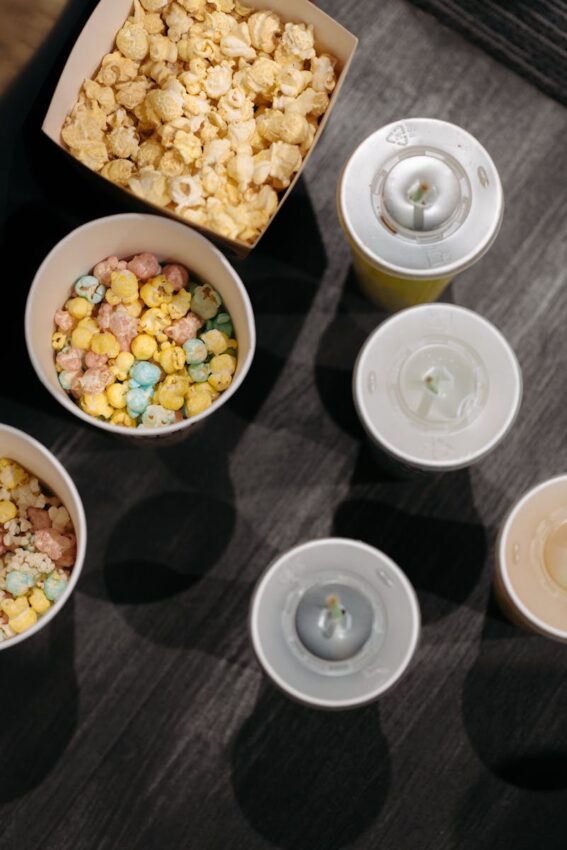 A flat lay image of colorful popcorn and drinks with lids, perfect for a movie night theme.