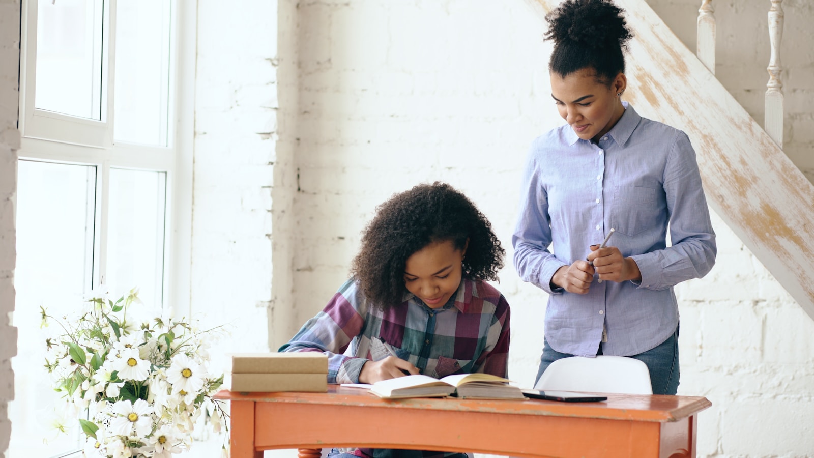 Woman helps girl with homework at desk.
