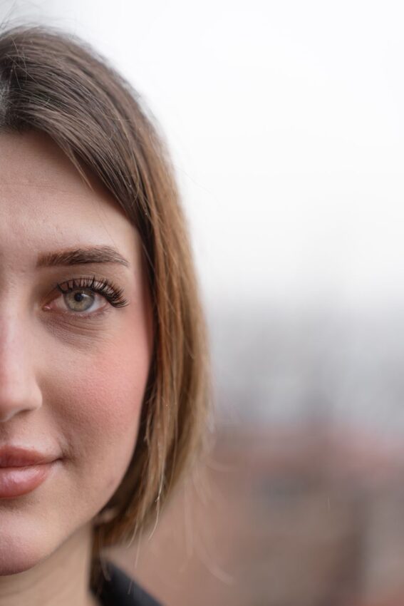 Half-face portrait of a young woman with brown hair and green eyes, outdoors against a blurred background.